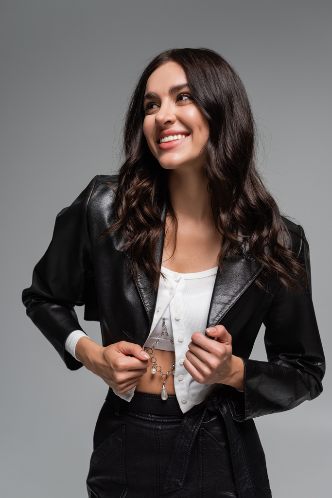 feliz jovem mulher ajustando jaqueta de couro preto isolado no cinza - Foto, Imagem