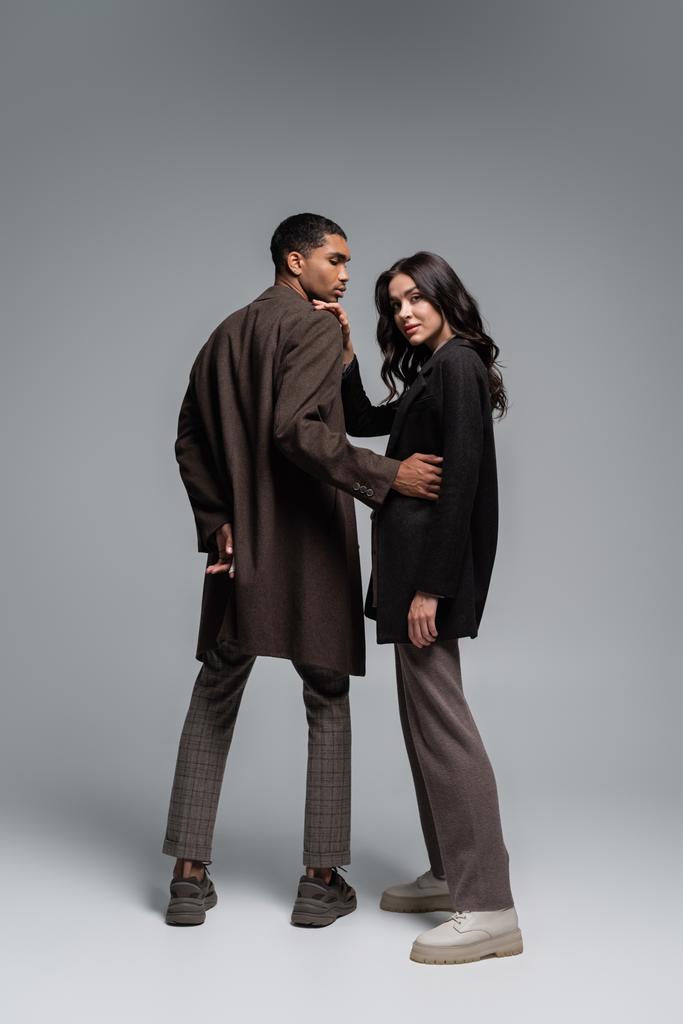 longitud completa de elegantes modelos interracial en ropa de moda otoñal posando en gris - Foto, Imagen