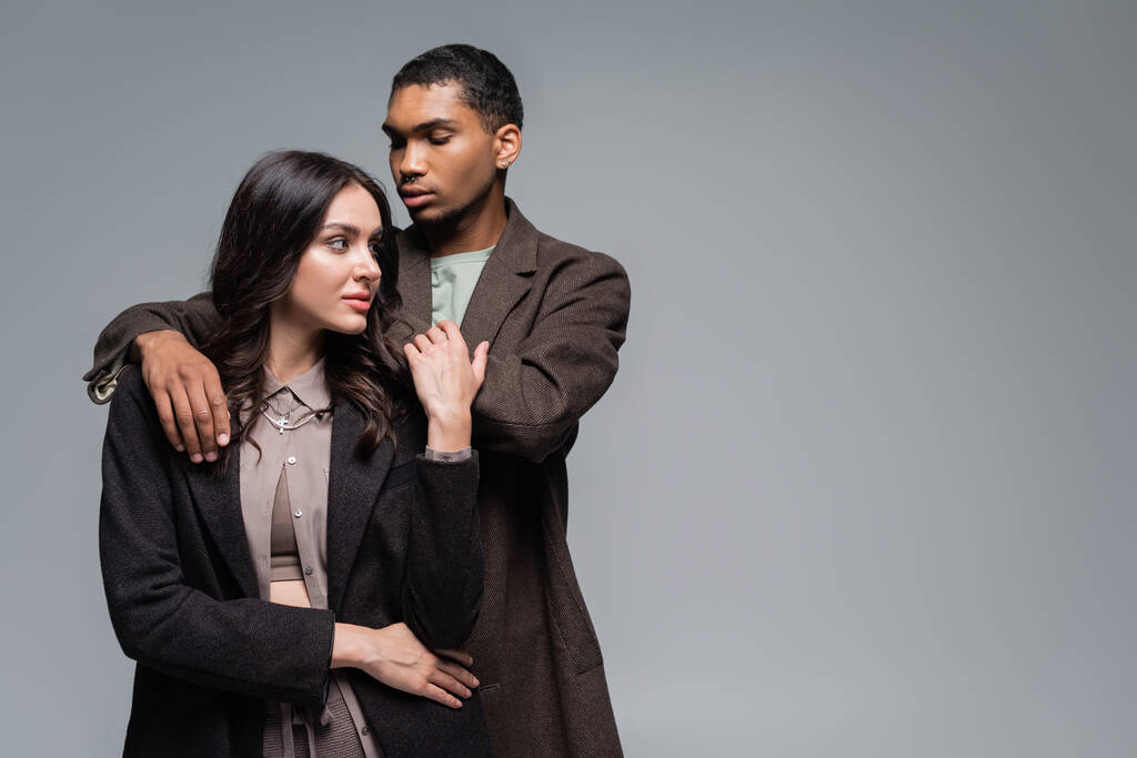 young african american man hugging brunette woman in blazer isolated on grey - Photo, Image