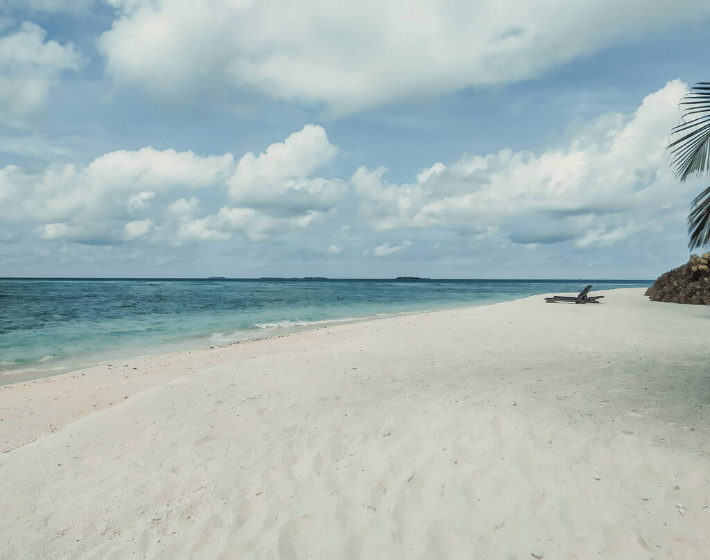 The deserted beach with empty sunbeds. Maldives, tropical island. A white sand, blue ocean and a blue sky. Summer vacation, luxury travel. Tranquility and relaxation. A picture in muted calm colors. - Photo, Image