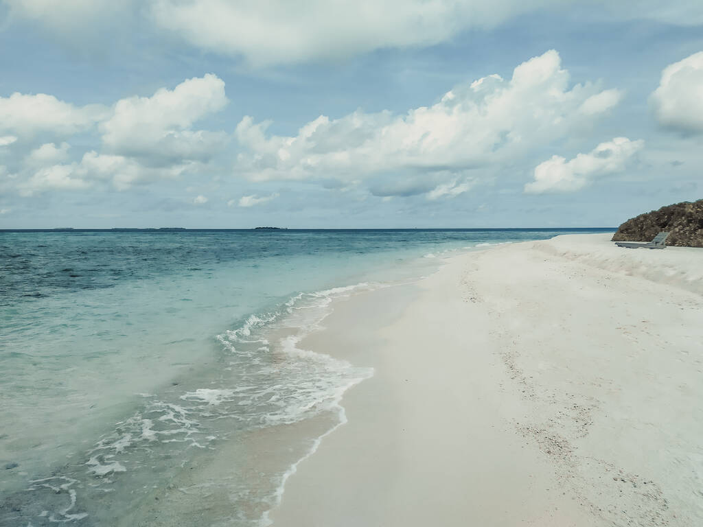 Der einsame Strand mit weißem Sand in der Nähe des türkisfarbenen Ozeans. Malediven, tropisches Paradies. Ruhe und Entspannung. Sommerurlaub, Luxusreisen. Schöner Meerblick in ruhigen gedeckten Farben. - Foto, Bild
