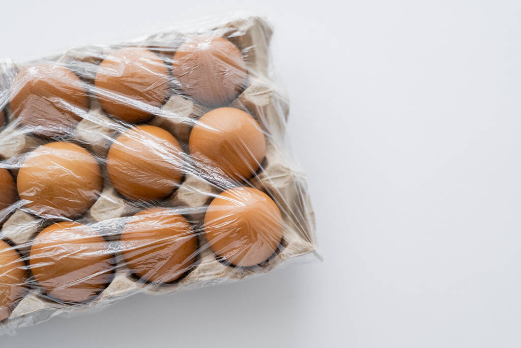 Top view of cellophane on brown eggs in tray on white background with copy space - Photo, Image