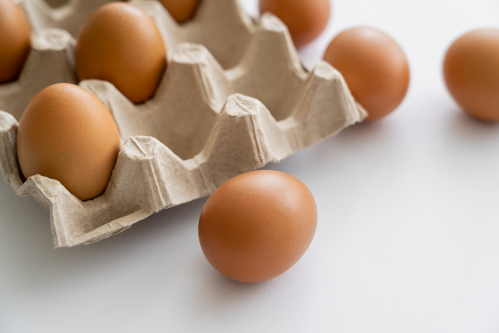 Vista de perto do ovo de galinha marrom perto da bandeja borrada no fundo branco  - Foto, Imagem