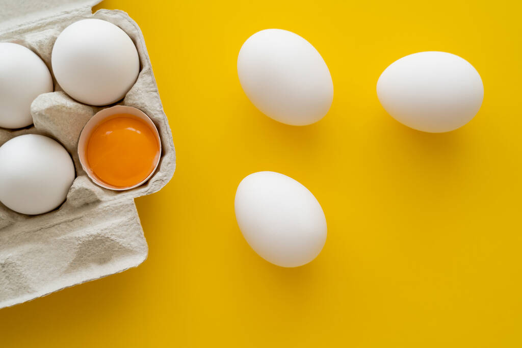 Horní pohled na vejce a žloutek ve skořápce v balení na žlutém pozadí  - Fotografie, Obrázek