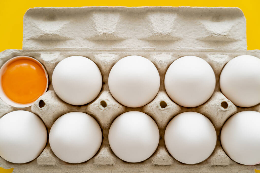 Top näkymä raaka keltuainen kuori lähellä munia pahvilaatikossa keltaisella pohjalla  - Valokuva, kuva