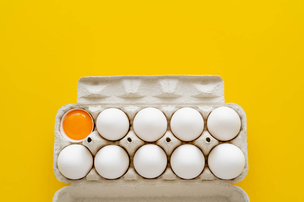 Vista superior de huevos y yema en cáscara en bandeja aislada en amarillo  - Foto, imagen