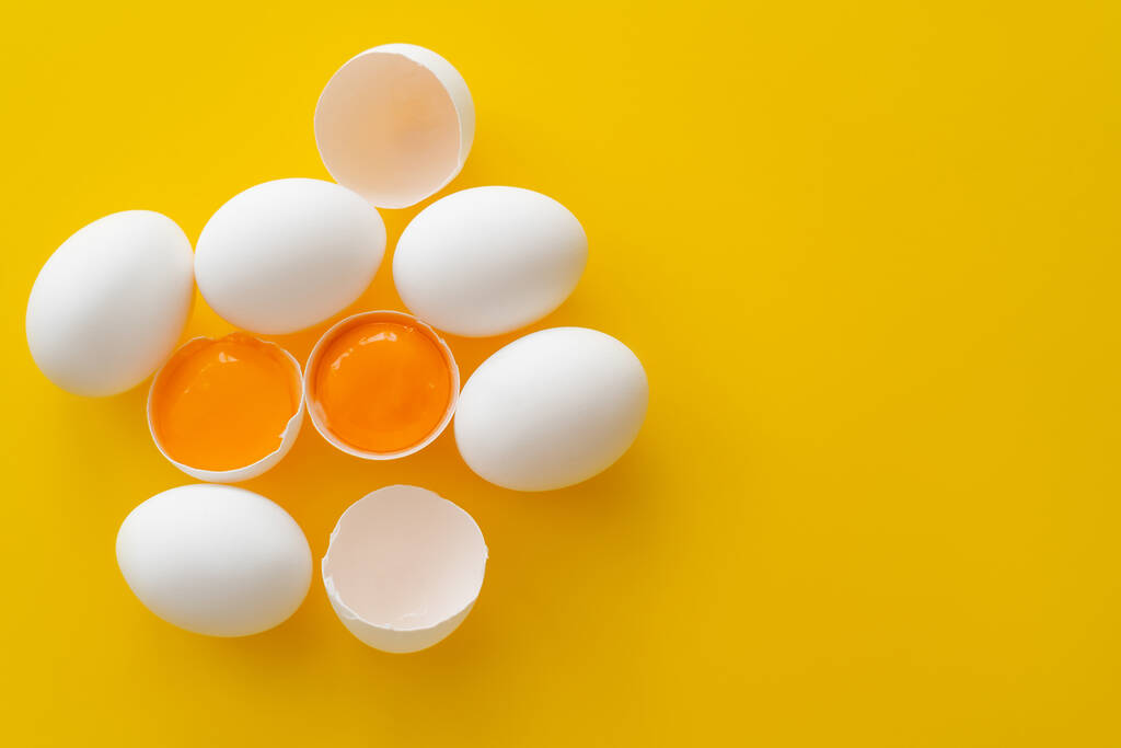 Vista superior de huevos y yemas en cáscaras sobre fondo amarillo  - Foto, Imagen