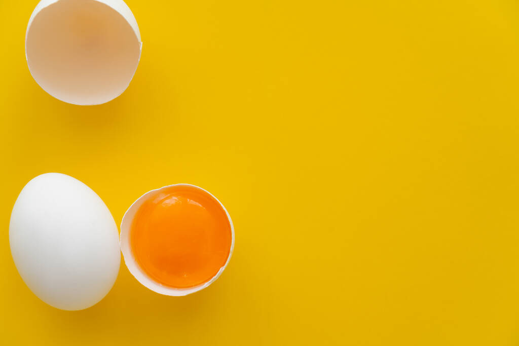 Draufsicht auf natürliches Eigelb in der Schale in der Nähe von weißem Ei auf gelbem Hintergrund  - Foto, Bild