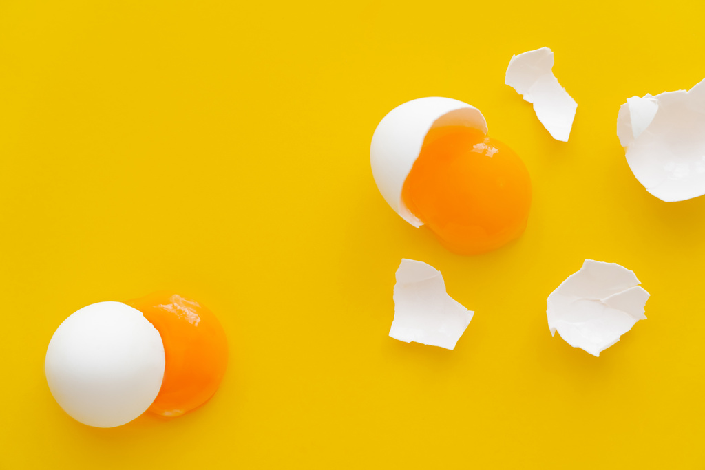 Horní pohled na žloutky a bílé vaječné skořápky na žlutém pozadí  - Fotografie, Obrázek