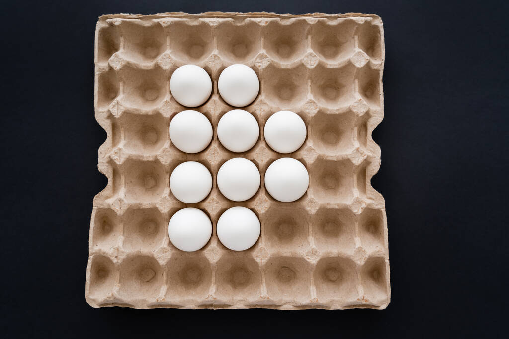 黒で隔離されたカートンパッケージの白い卵のトップビュー  - 写真・画像