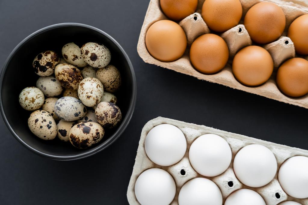 Top kilátás csirke és fürj tojás tálban és konténerek fekete alapon  - Fotó, kép