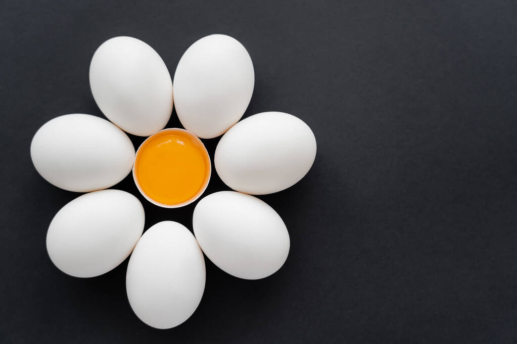 Colocação plana de gema crua com casca perto de ovos de galinha no fundo preto  - Foto, Imagem