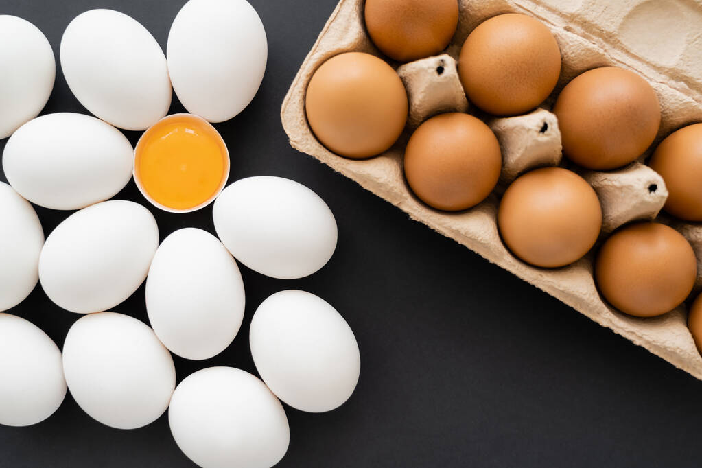 Вид сверху коричневых и белых куриных яиц возле картонного трапа на чёрном фоне  - Фото, изображение