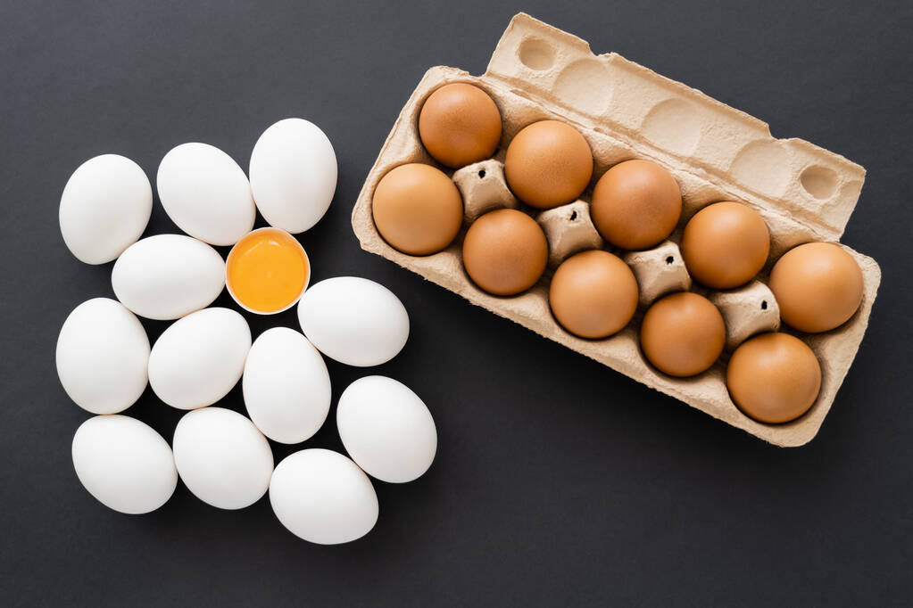 Top näkymä orgaaninen keltuainen kuori lähellä munia pahvipakkauksessa mustalla pohjalla  - Valokuva, kuva