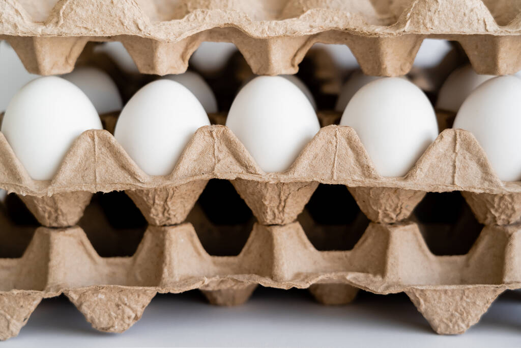 Αυγά μεταξύ εμπορευματοκιβωτίων από χαρτόνι σε λευκό φόντο  - Φωτογραφία, εικόνα