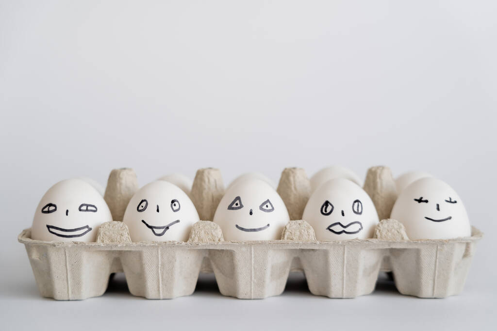 Розфарбовані курячі яйця з виразами обличчя в лотку на білому тлі
  - Фото, зображення