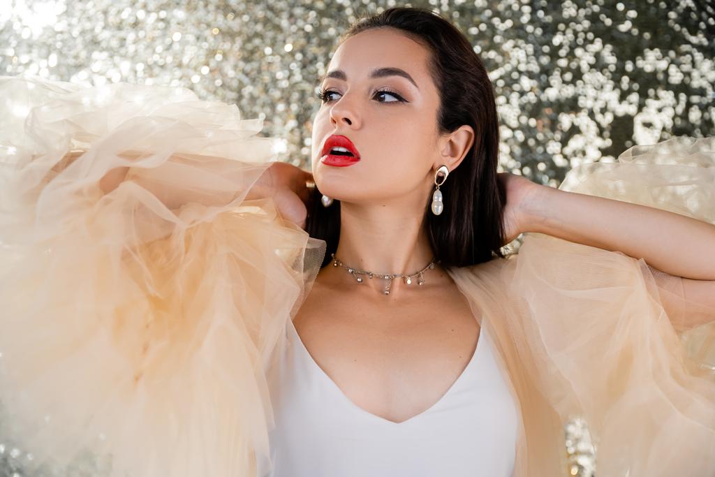 young woman with red lips posing in elegant chiffon dress and looking away on shiny background - Photo, Image