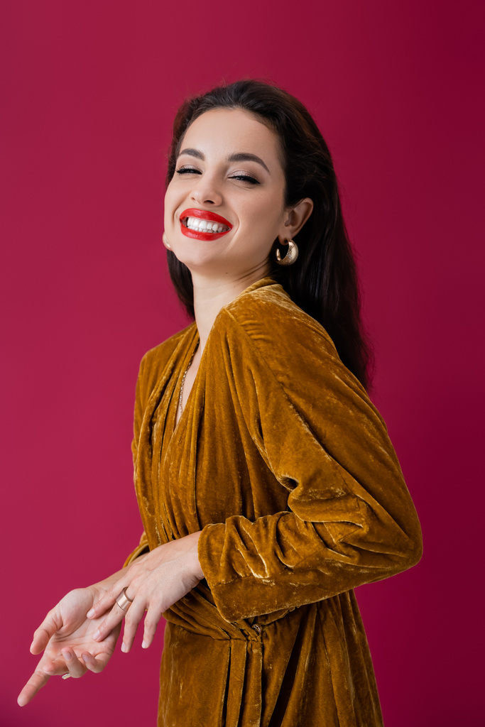 stylish woman in elegant velour dress laughing at camera isolated on red - Photo, Image