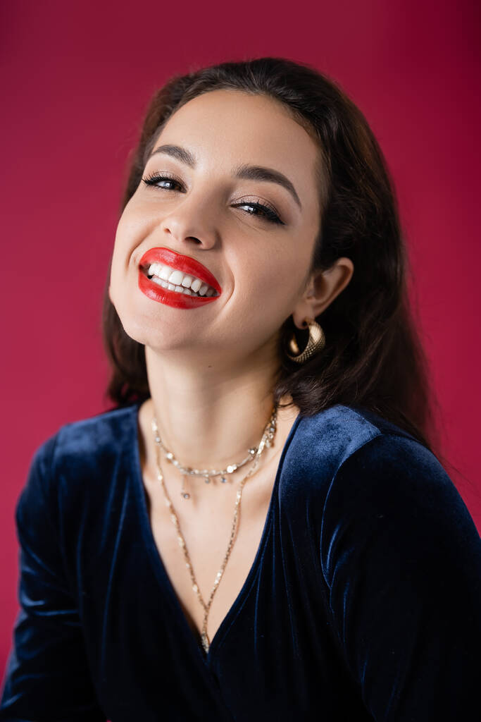 portrait of happy elegant woman with makeup smiling at camera isolated on red - Photo, Image