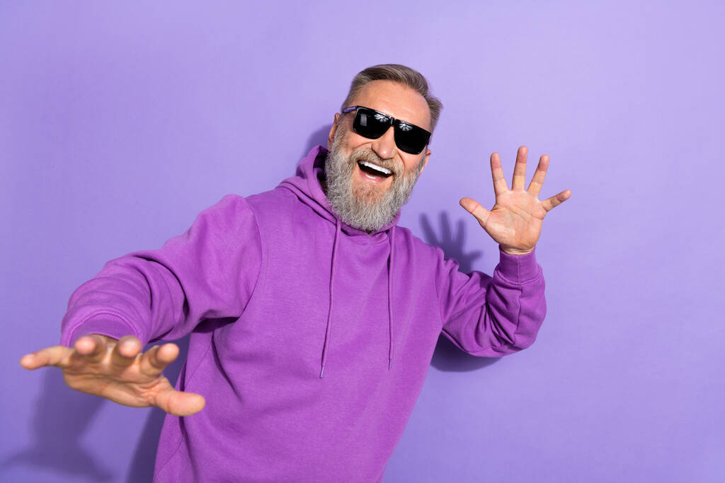 Foto de un hombre guapo y despreocupado con barba gris blanca usar sudadera púrpura demostrar mano aislada sobre fondo de color violeta. - Foto, imagen