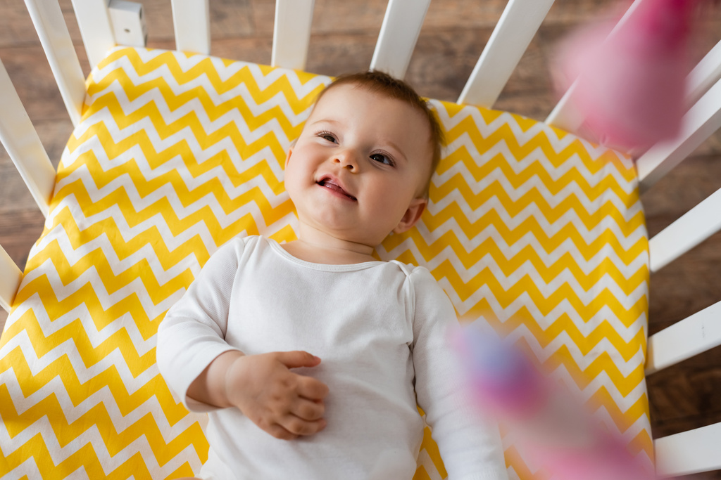 vrchní pohled na kojeneckou dívku v bílém baby romper ležící na žluté lůžkoviny v postýlce  - Fotografie, Obrázek