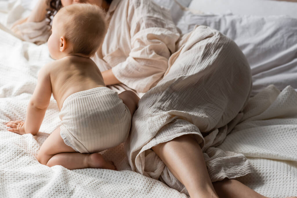 przycięty widok matki w odzieży loungewear leżącej w pobliżu córeczki na łóżku - Zdjęcie, obraz
