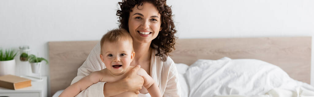 mujer alegre en ropa de salón sosteniendo en brazos hija bebé sorprendido con la boca abierta, pancarta - Foto, imagen