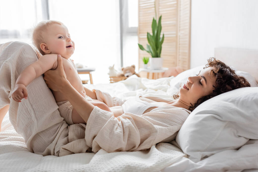 felice donna in loungewear sdraiato sul letto con la figlia bambino carino  - Foto, immagini
