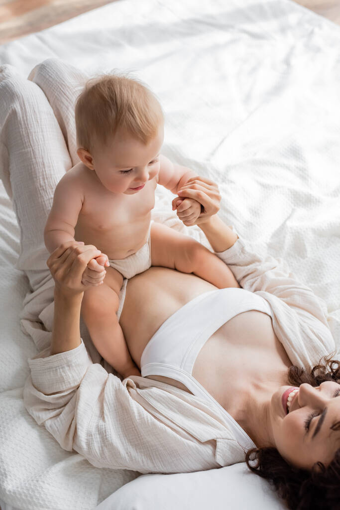 вид зверху щасливої жінки в вітальні лежить на ліжку і тримає руки немовляти дочки
  - Фото, зображення