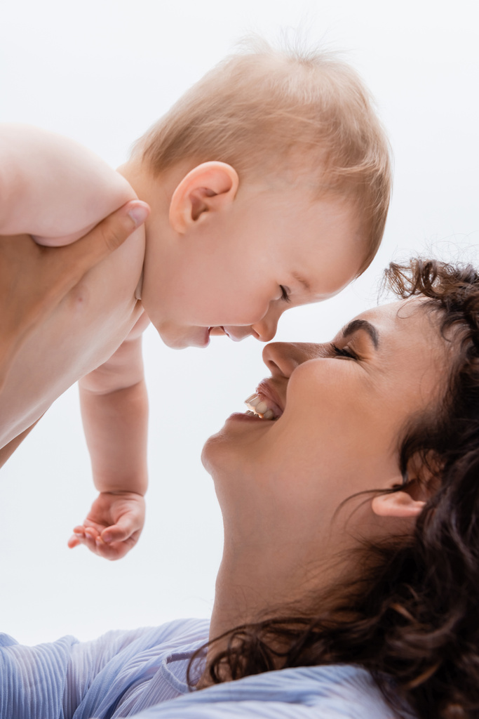 Portret pozytywnej matki trzymającej dziecko od nosa do nosa wyizolowane na białym - Zdjęcie, obraz