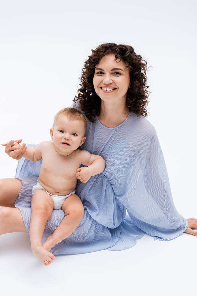 Happy woman holding hand of baby daughter and sitting on white background  - Photo, Image