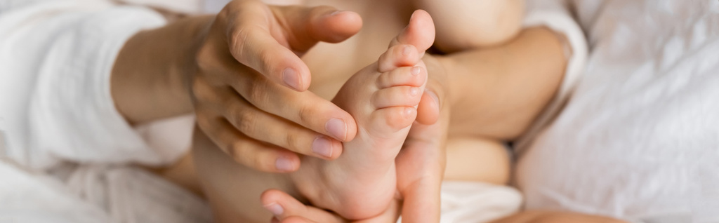Cropped view of woman touching foot of infant daughter on blurred bed, banner  - Photo, Image