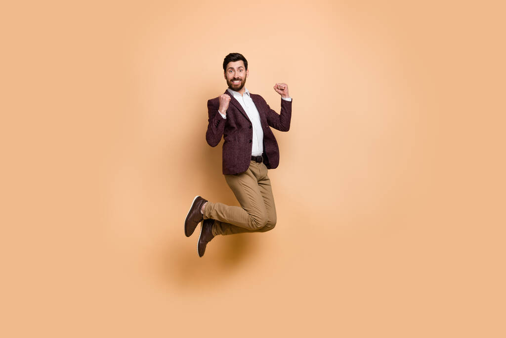 Imagen completa del hombre de negocios encantado y lleno de alegría saltando en la emoción aislado sobre un fondo de color beige. - Foto, Imagen
