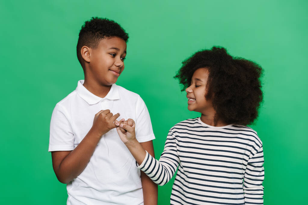 Fekete fiú és lány horogra akasztják egymás kis ujjait békülésben elszigetelve a zöld háttér felett - Fotó, kép
