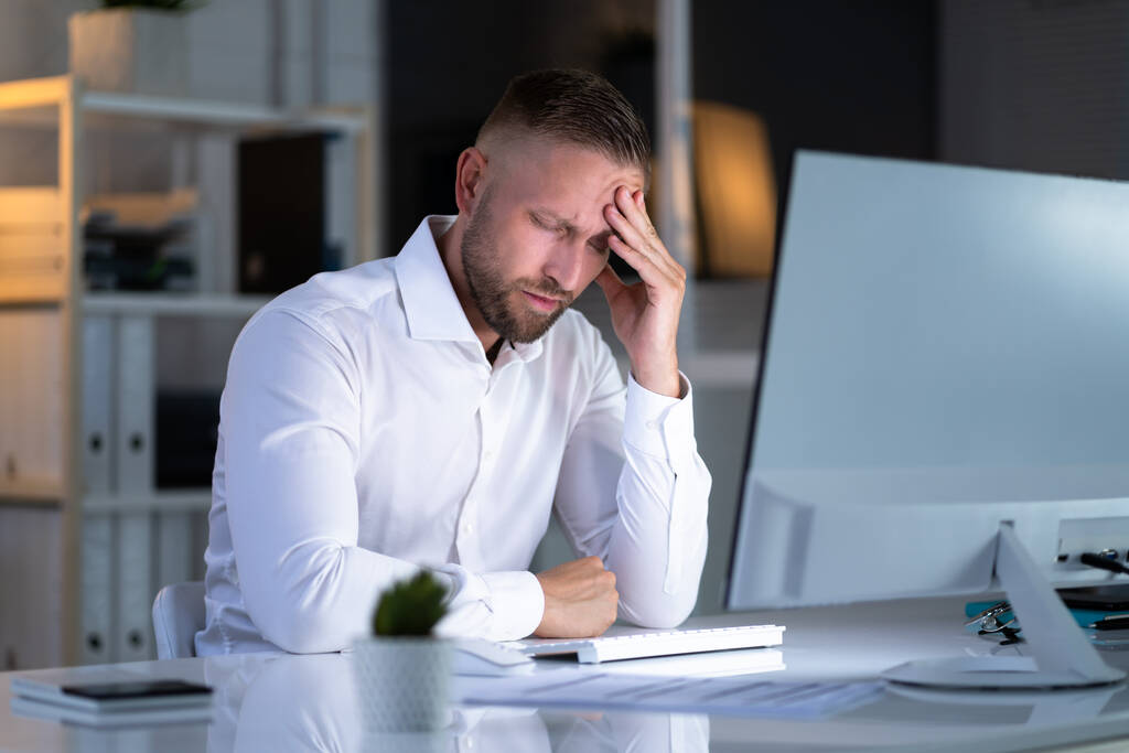 Стрессовый бизнесмен работает допоздна над ноутбуком в офисе - Фото, изображение
