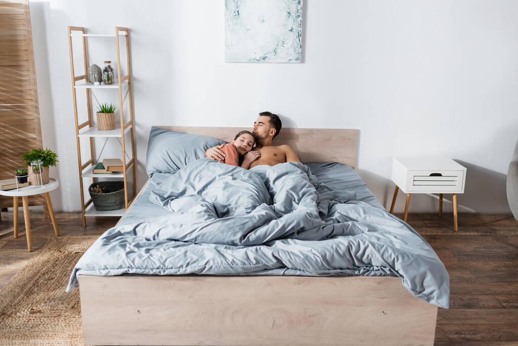 young woman sleeping near shirtless man under grey blanket in modern bedroom - Photo, Image