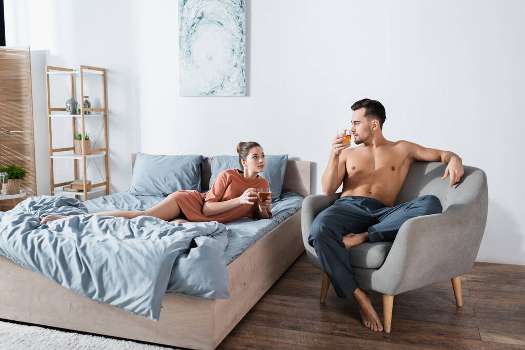 junges Paar schaut einander beim Teetrinken im modernen Schlafzimmer an - Foto, Bild