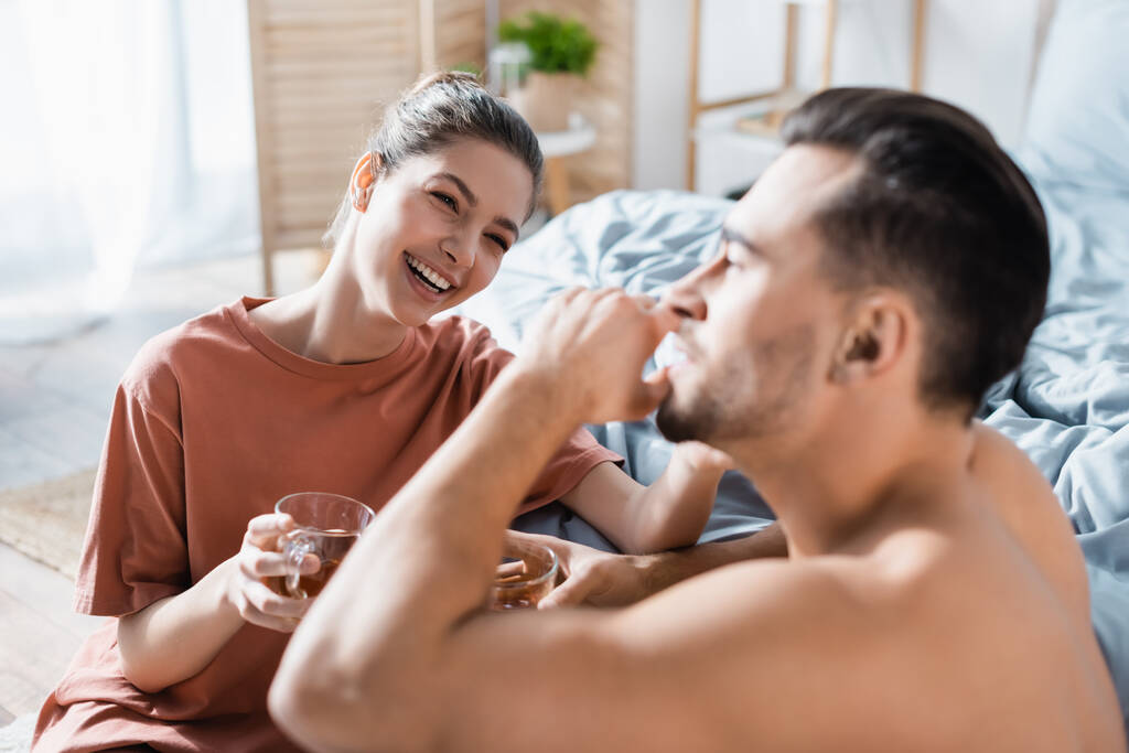 jeune femme joyeuse avec une tasse de thé en regardant son petit ami au premier plan flou - Photo, image