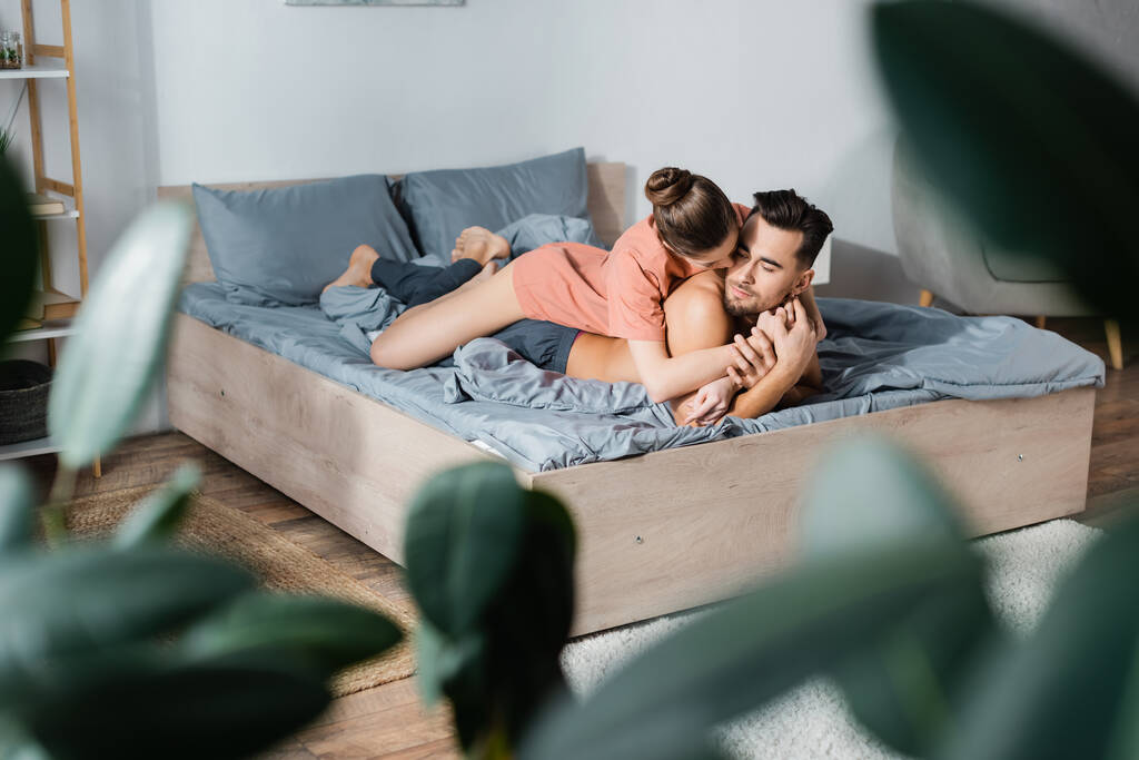 сексуальная женщина обнимает парня без рубашки лежащего на кровати на размытом переднем плане - Фото, изображение