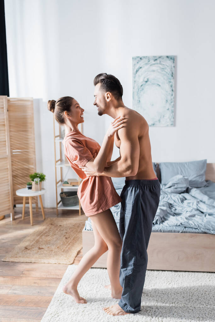 side view of happy young couple smiling and dancing in bedroom - Photo, Image