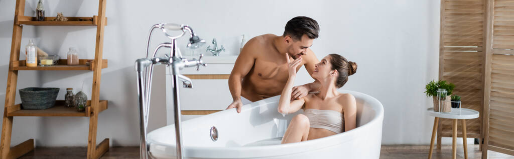 donna seducente che si rilassa nella vasca da bagno e tocca il viso del fidanzato muscolare sexy, banner - Foto, immagini