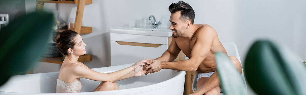 jonge vrouw in bad en sexy shirtloze man hand in hand en kijken naar elkaar, banner - Foto, afbeelding