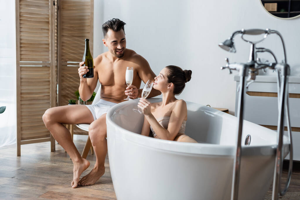 heureux et sexy couple tenant des verres de champagne et parler dans la salle de bain - Photo, image