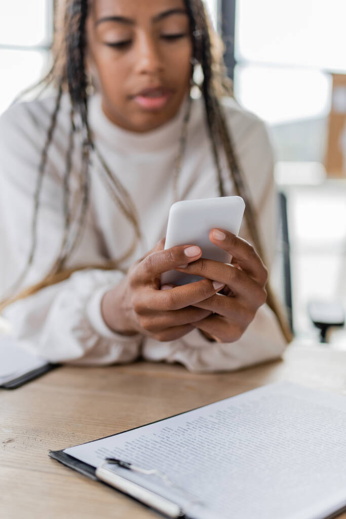Homályos afro-amerikai üzletasszony használja okostelefon közelében vágólap az irodában  - Fotó, kép