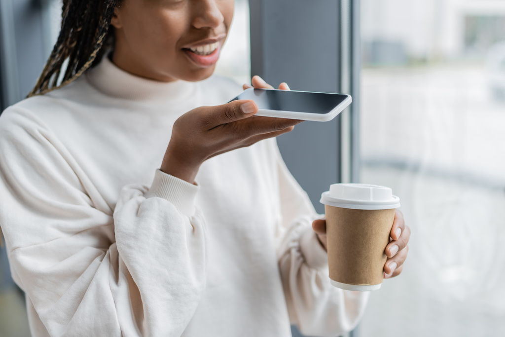 Ausgeschnittene Ansicht einer afrikanisch-amerikanischen Geschäftsfrau, die Sprachnachrichten aufzeichnet und Kaffee hält, um ins Büro zu gehen  - Foto, Bild