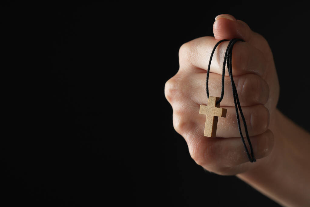 Mujer sosteniendo cruz cristiana de madera sobre fondo negro, primer plano. Espacio para texto - Foto, Imagen