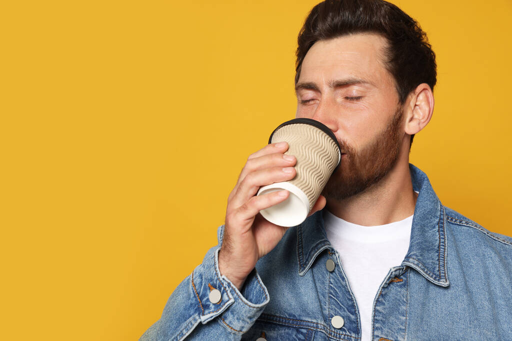 Бородатый мужчина пьет кофе на оранжевом фоне. Пространство для текста - Фото, изображение