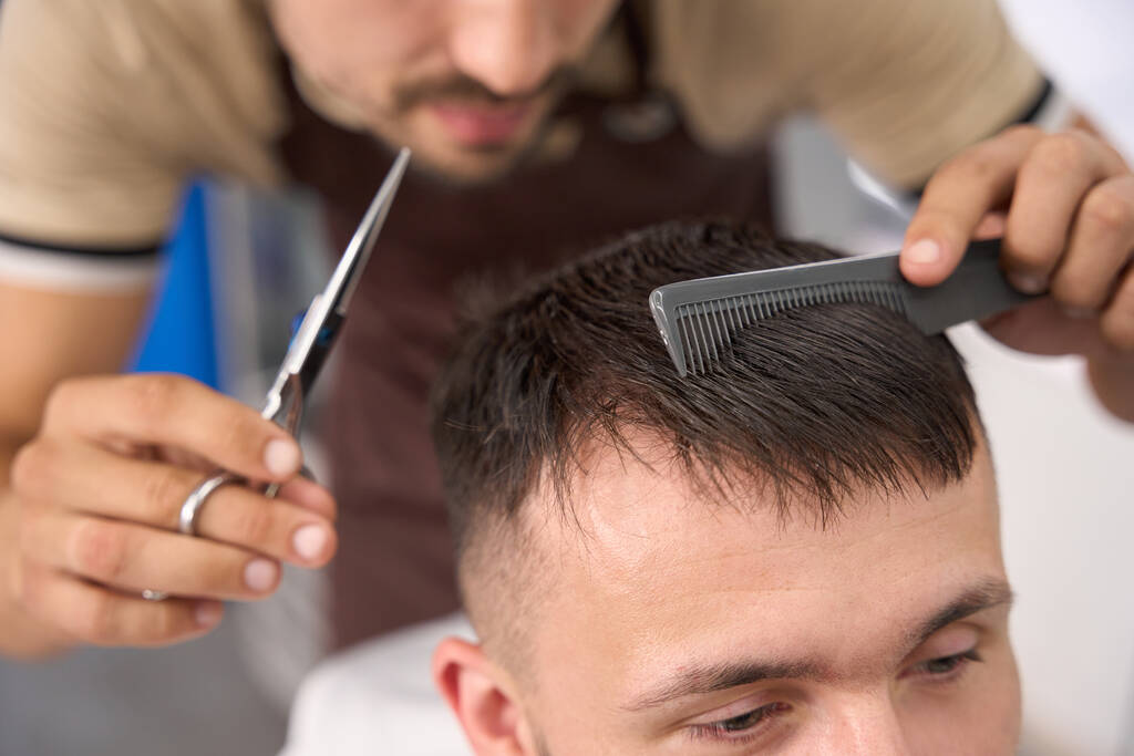 Cropped photo of dedicated barber combing client hair while preparing to give it a fresh cut - Photo, Image