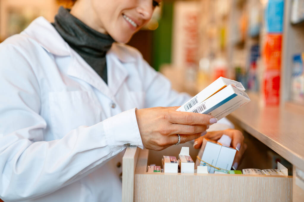 Bílý lékárník v laboratorním plášti s úsměvem při práci v lékárně - Fotografie, Obrázek
