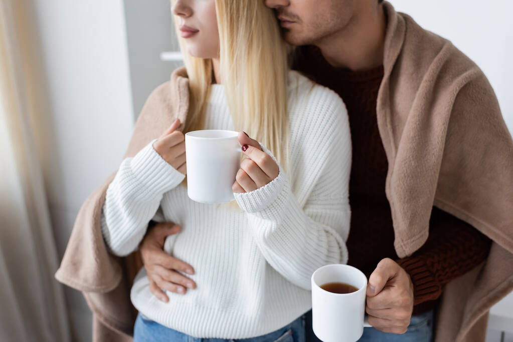 kivágott kilátás fiatal pár borított takaró ölelés, miközben a kezében csésze teát otthon - Fotó, kép